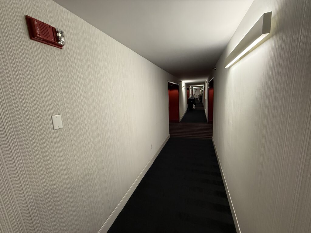 A plain hotel hallway with dark carpet and white walls. Doorframes are a bright red.