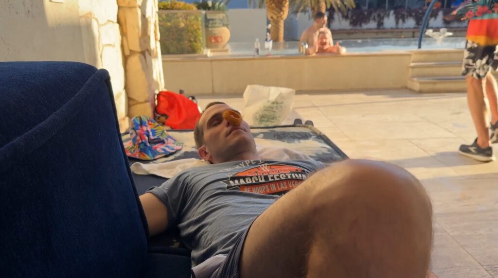 My brother, laying on a couch in a cabana, sleeping, with an onion ring on his nose.