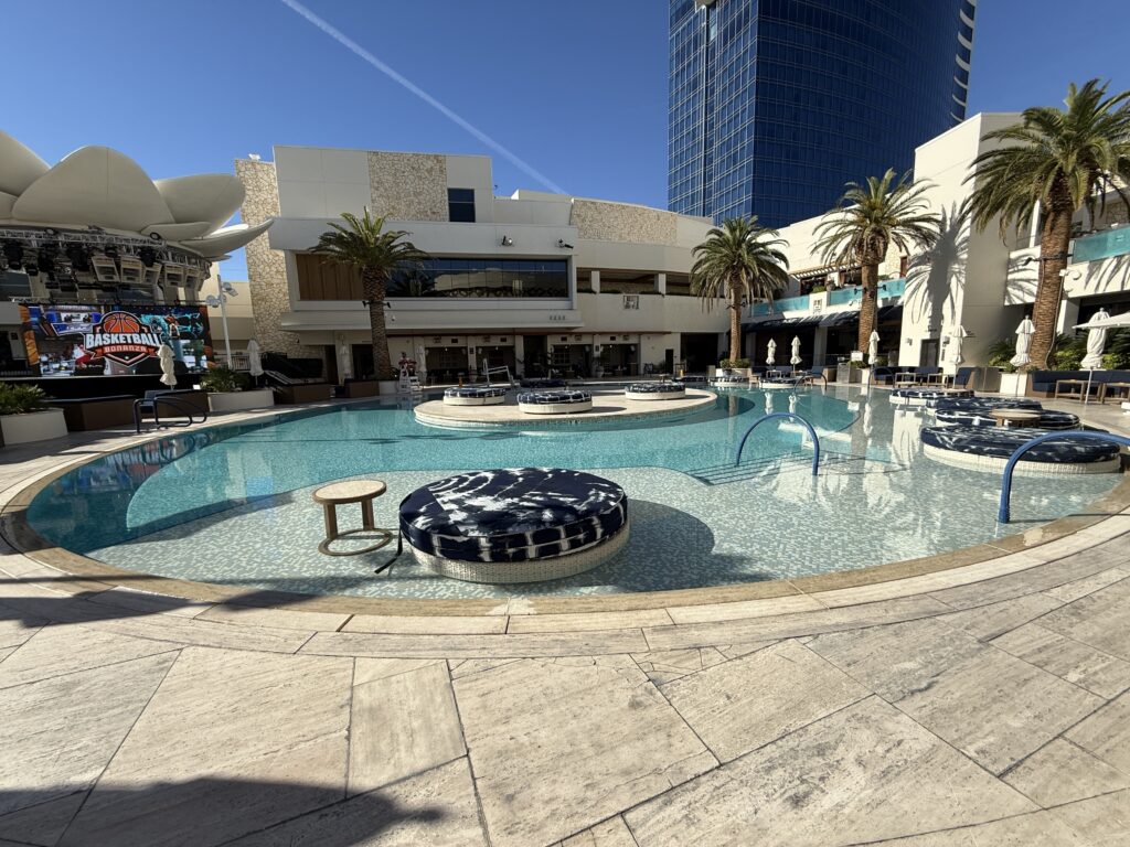 A pool with submerged daybeds, with the baskeball viewing screen on the left.