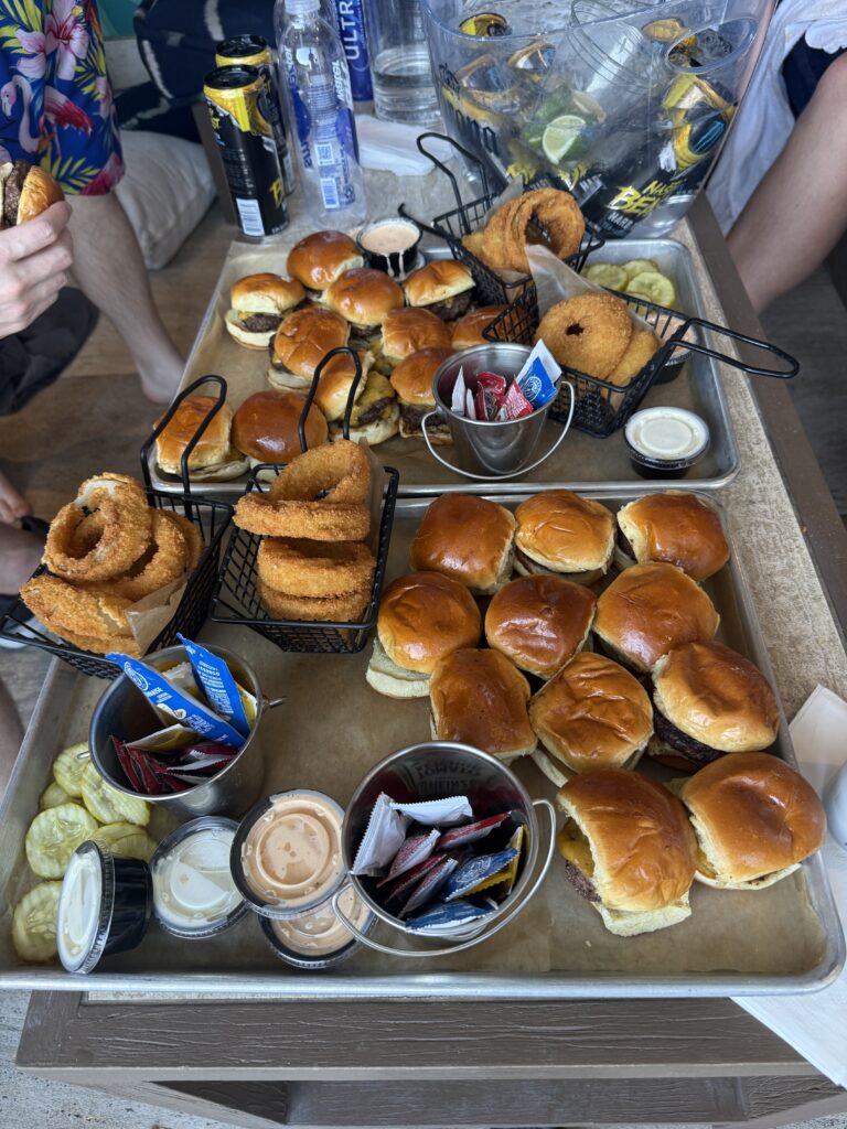 A tray full of about 25 sliders with 4 stacks of onion rings accompanying them.