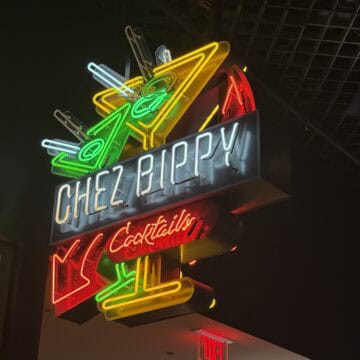 A neon sign hanging above Luchini depicting cocktail glasses that says "Chez Bippy Cocktails".