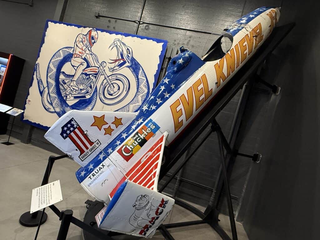 Evel Knievel's Skycycle on a ramp in front of a promotional poster for the Snake River Jump.