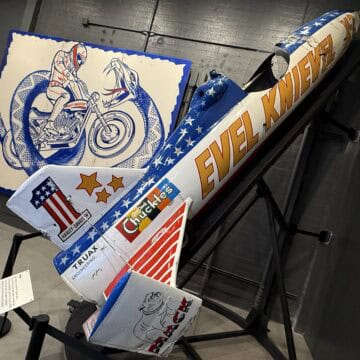 Evel Knievel's Skycycle on a ramp in front of a promotional poster for the Snake River Jump.