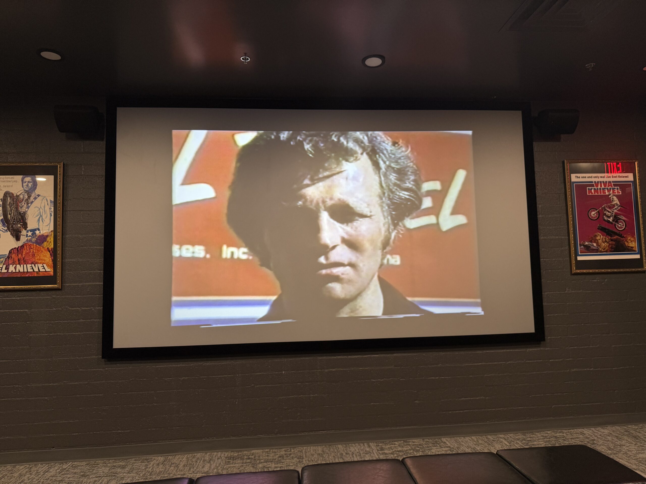 A theater screen showing an informational video on Evel Knievel.