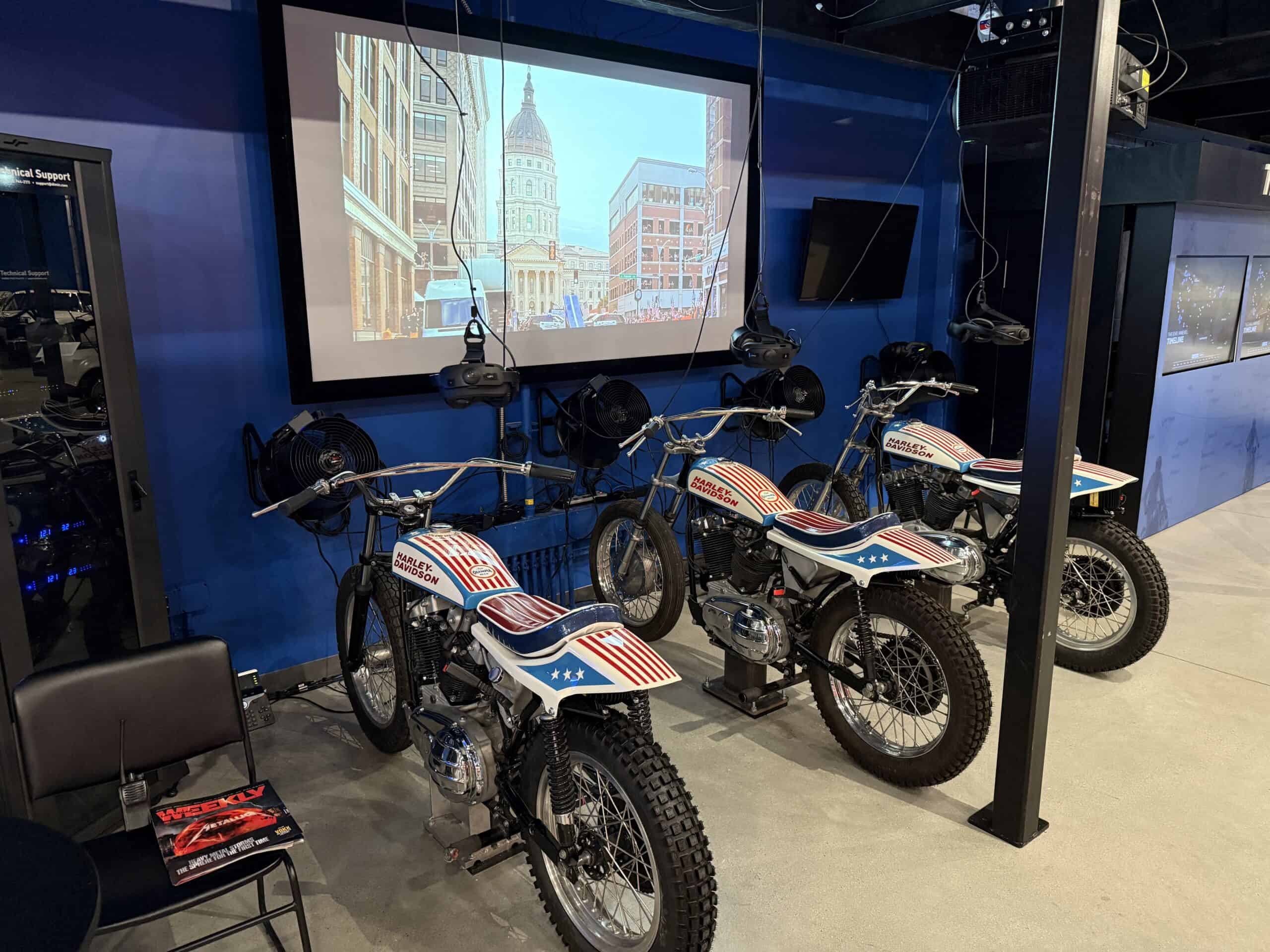 MOtorcycles lined up with VR headsets hanging overhead and air fans in front of them.