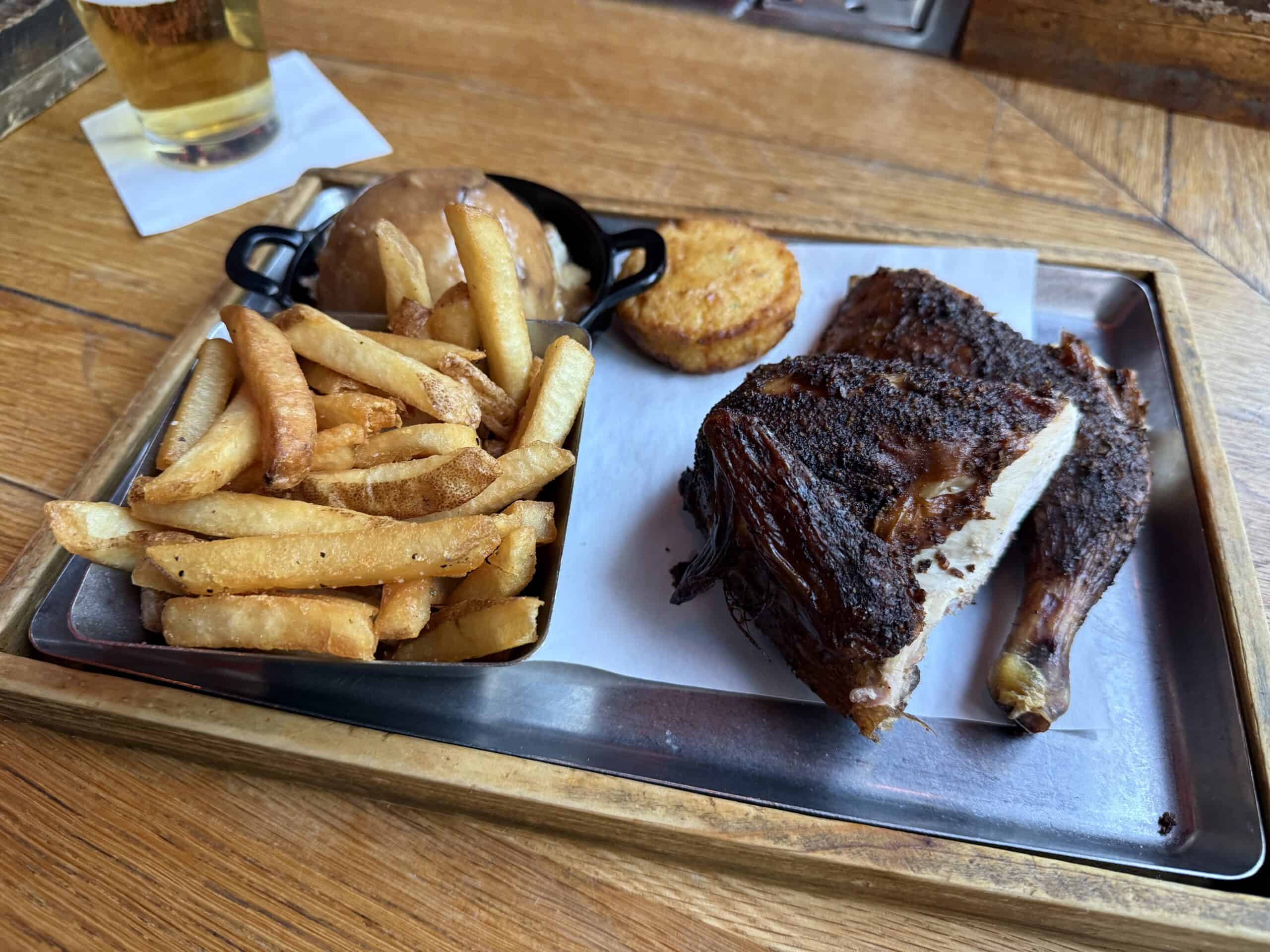 Half chicken plate next to french fries, mashed potatoes, and a cornbread biscuit.