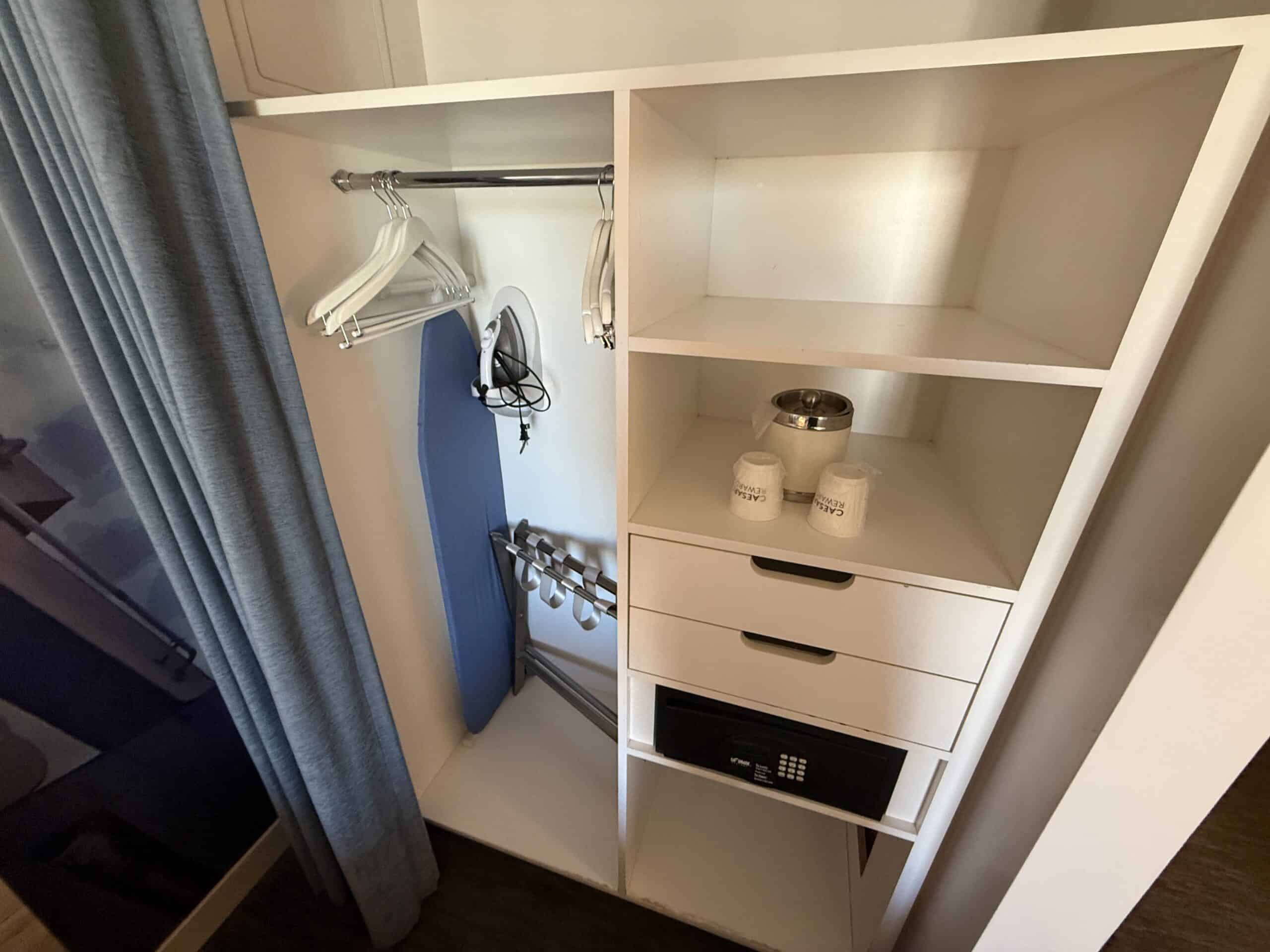 An open closed stocked with hangers, iron, ironing board, and a safe.
