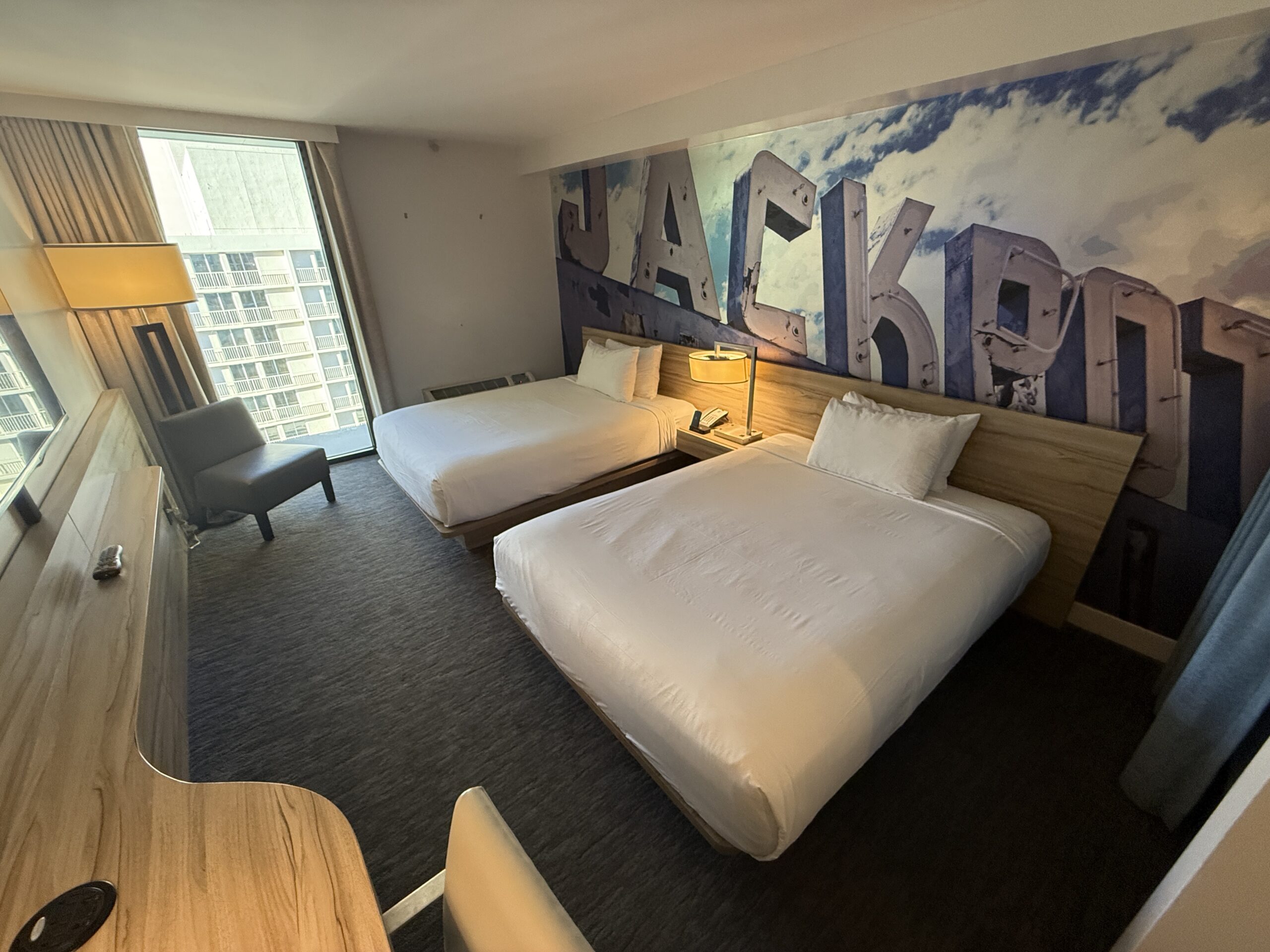 A wide angle view of the room, with two beds pushed up against a decorative accent wall that says "Jackpot".