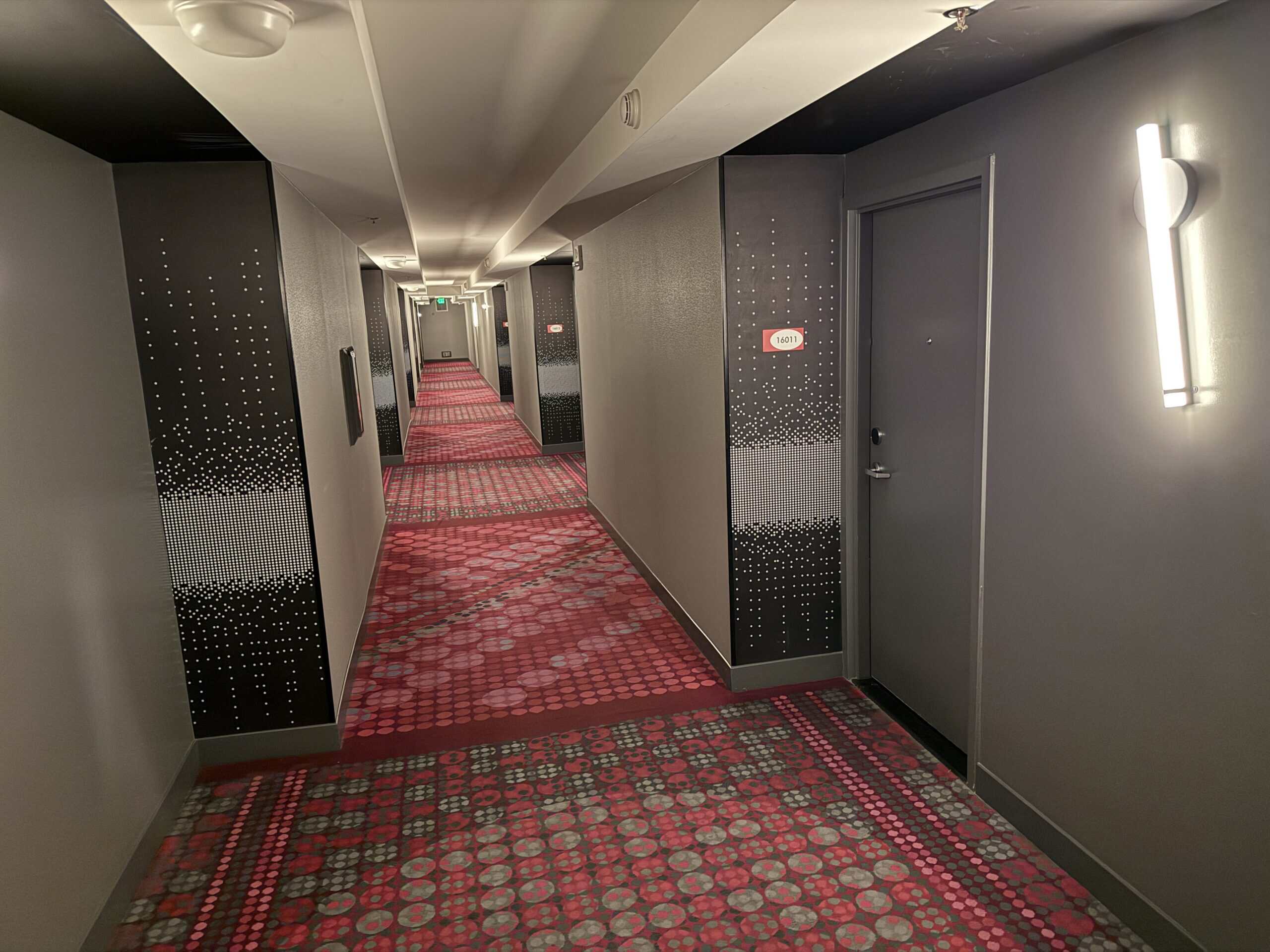 A well lit hotel hallway with dark walls and red carpeting.