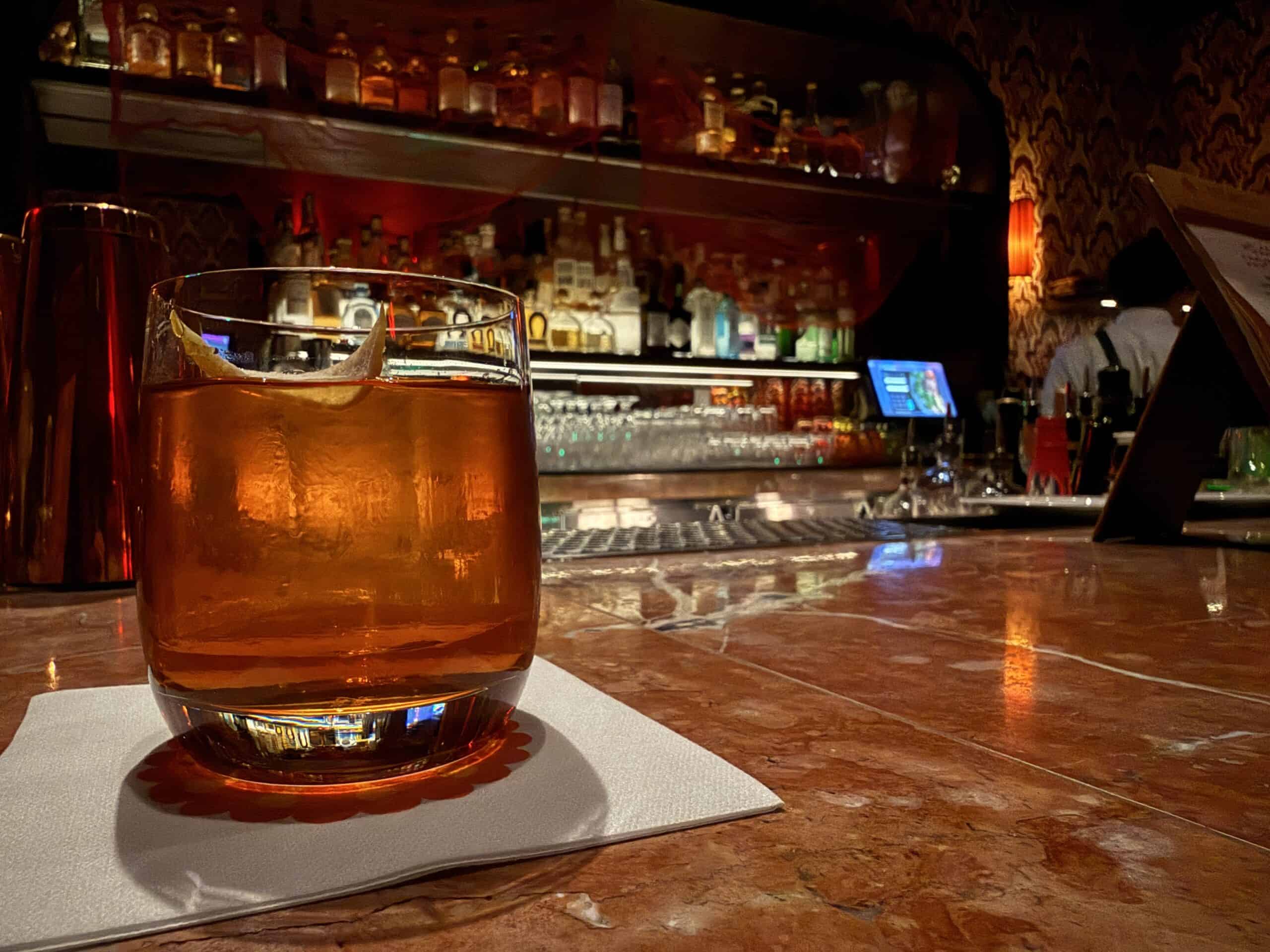 My old fashioned, sitting on the bar. The illuminated bottles on the bar's back wall are blurry in the background.