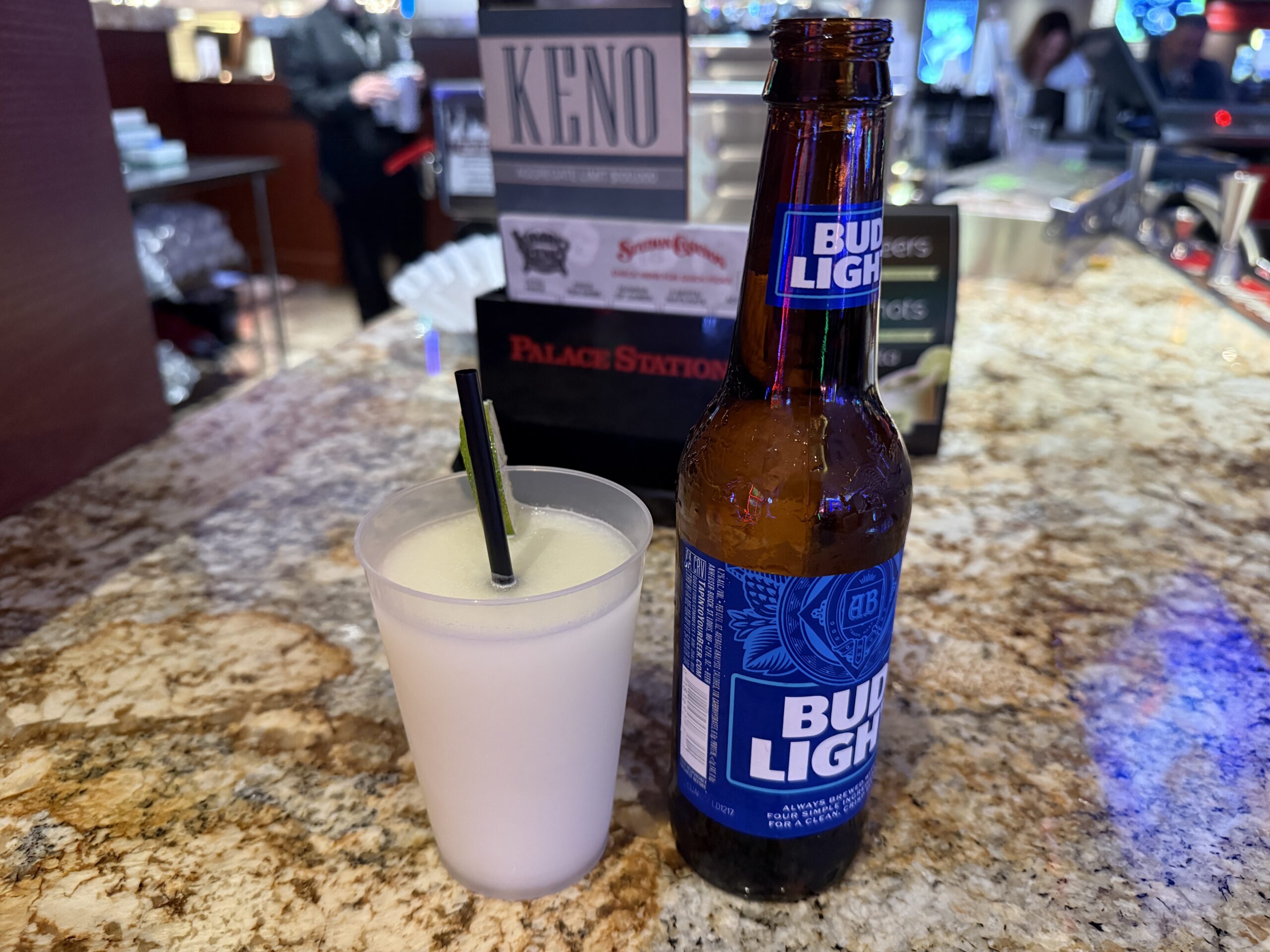 A blended margarita next to a bottle of Bud LIght.