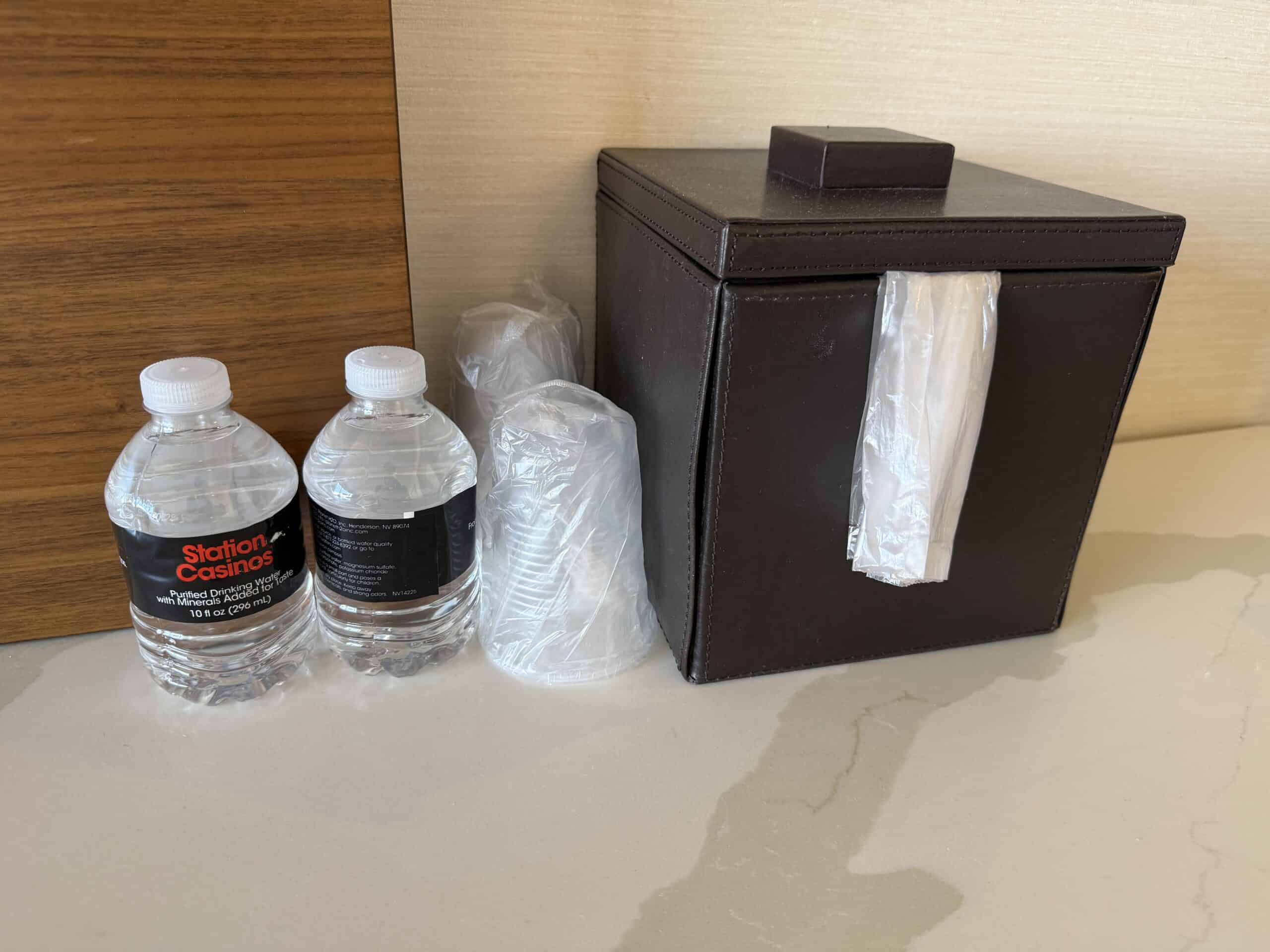 A couple of comp bottles of water next to a leather ice bucket and plastic cups.