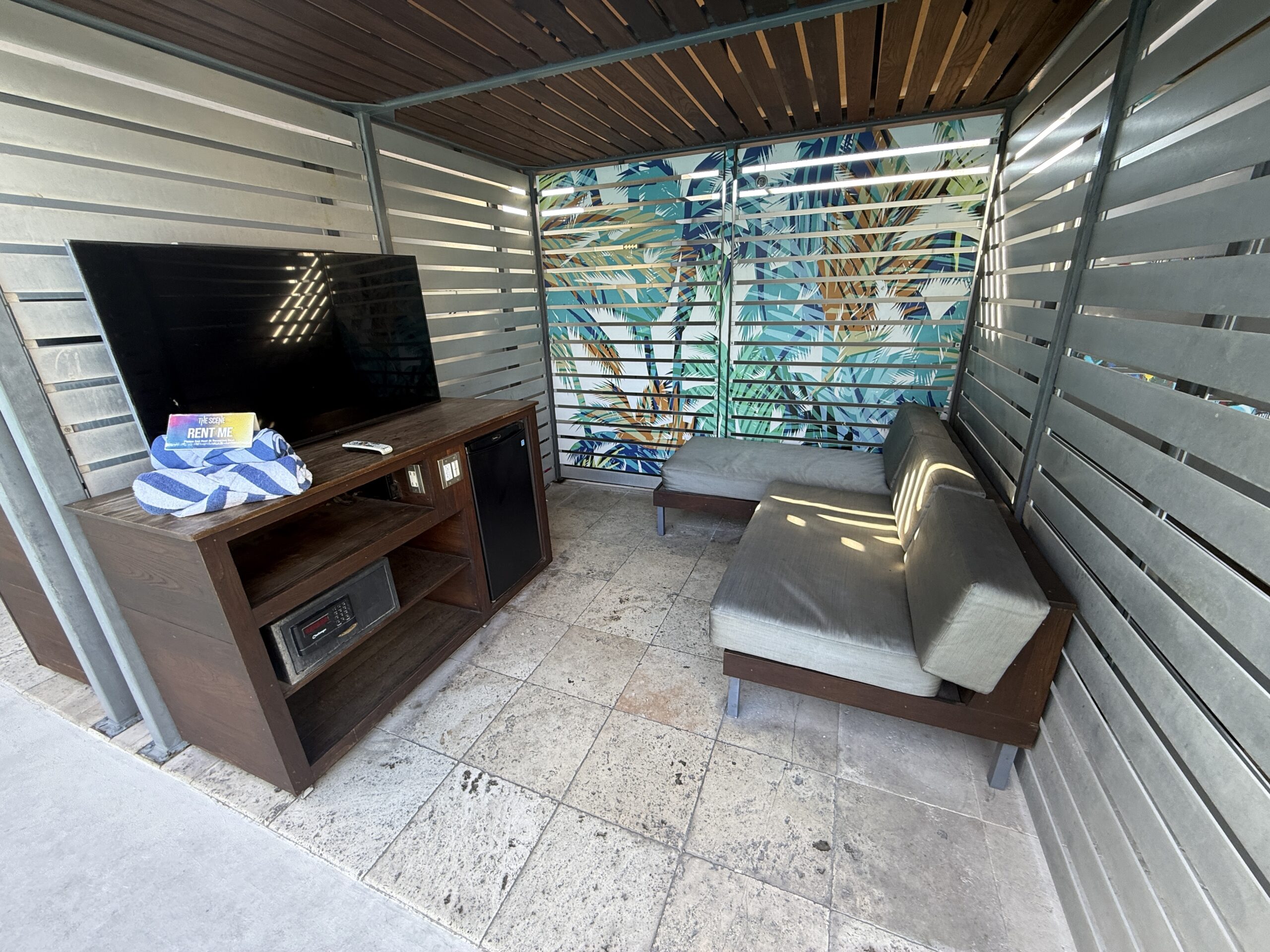 A pool cabana with a padded couch pointed at a TV.