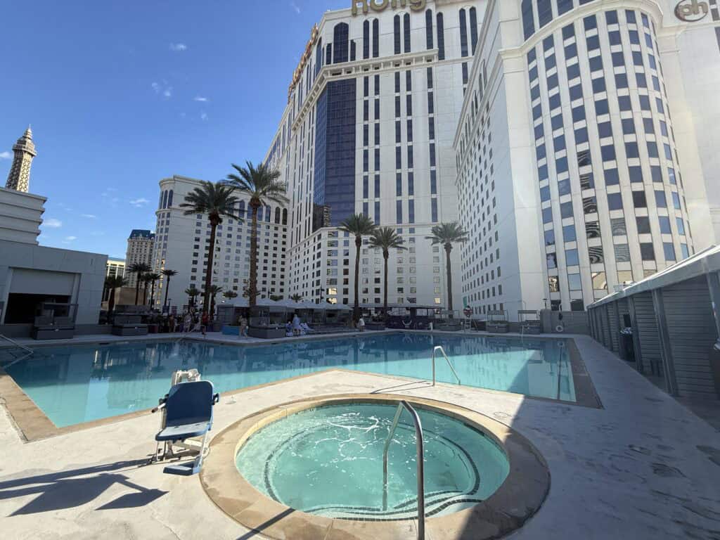 A hot tub in front of a large standard pool behind it. Planet Hollywood's hotel tower is in the background.