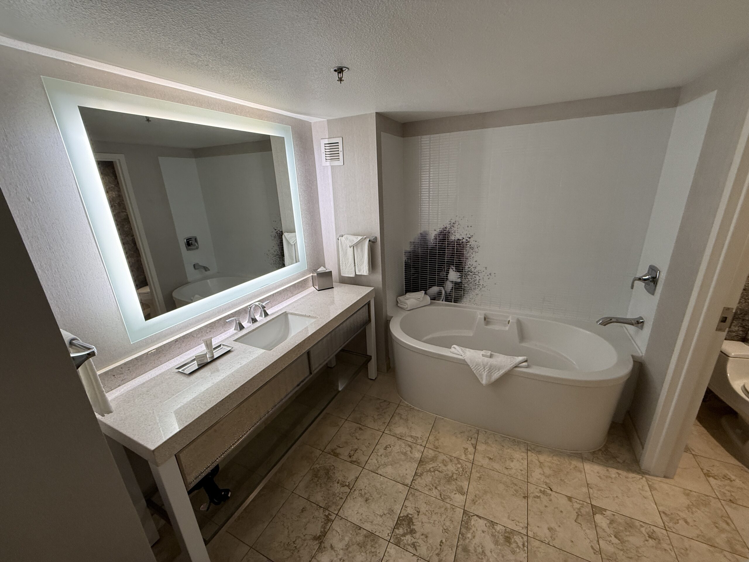 An illuminated mirror over a single sink vanity. To the right is a stand alone deep tub.