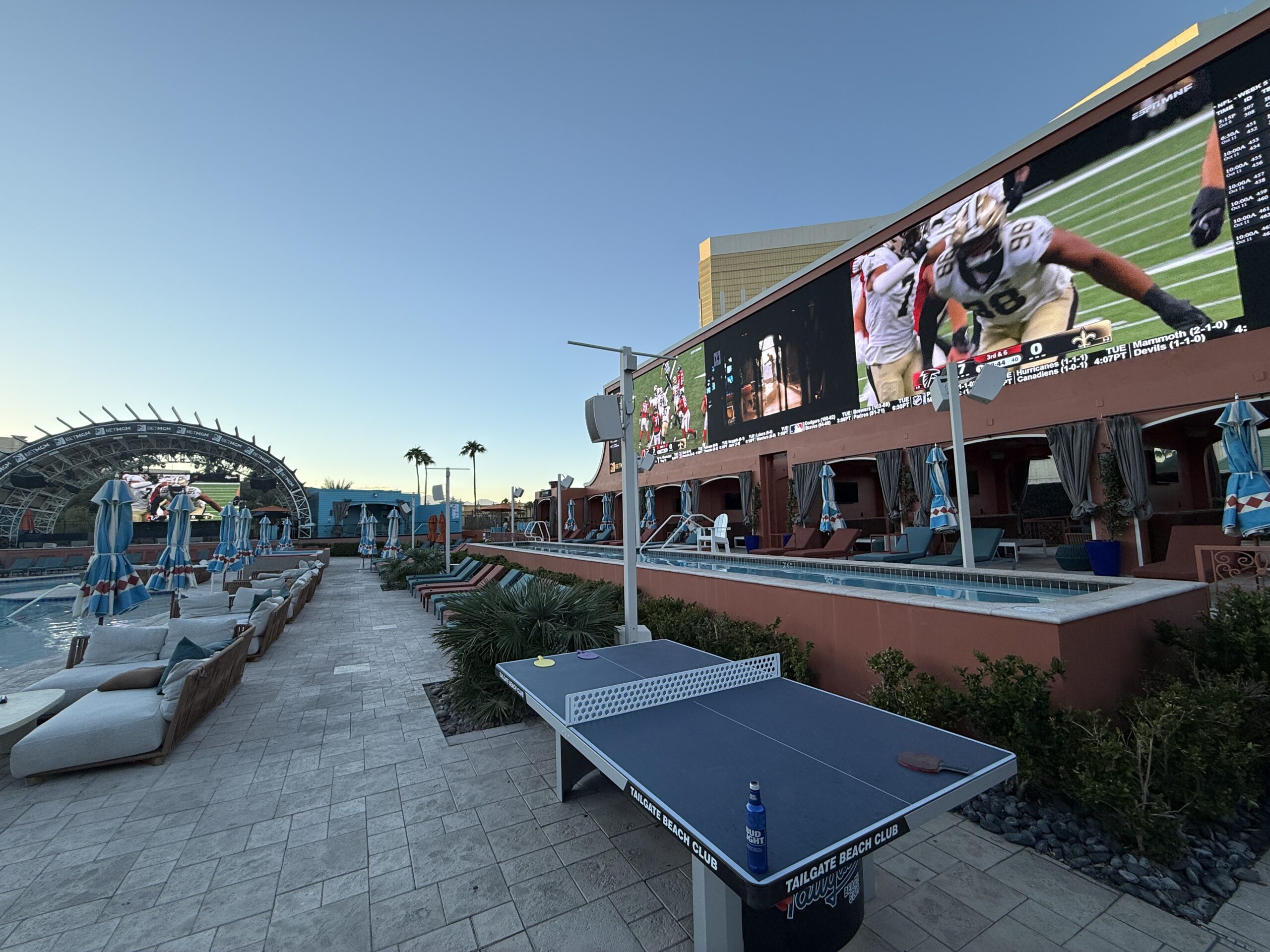 A large, rectangular screen playing football with a ping pong table in the goreground.