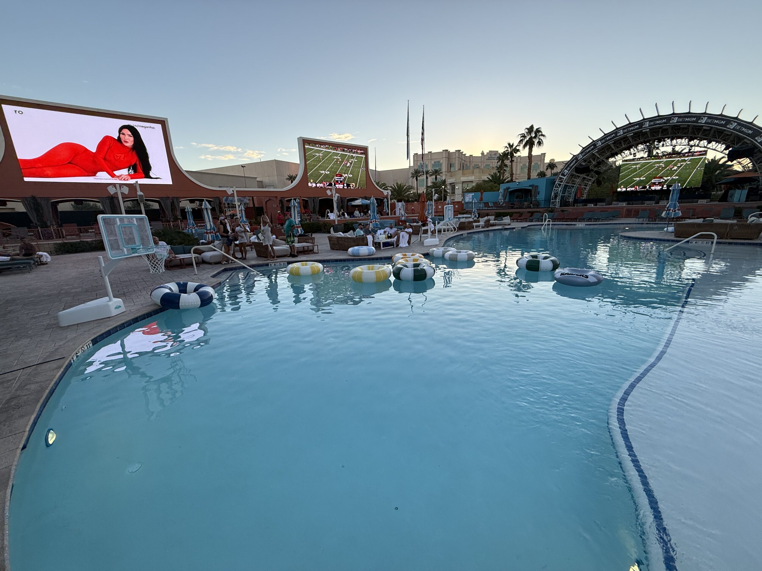 A wide angle shot of Tailgate Beach Club, with a swimming pool in the foreground and screens behind it.