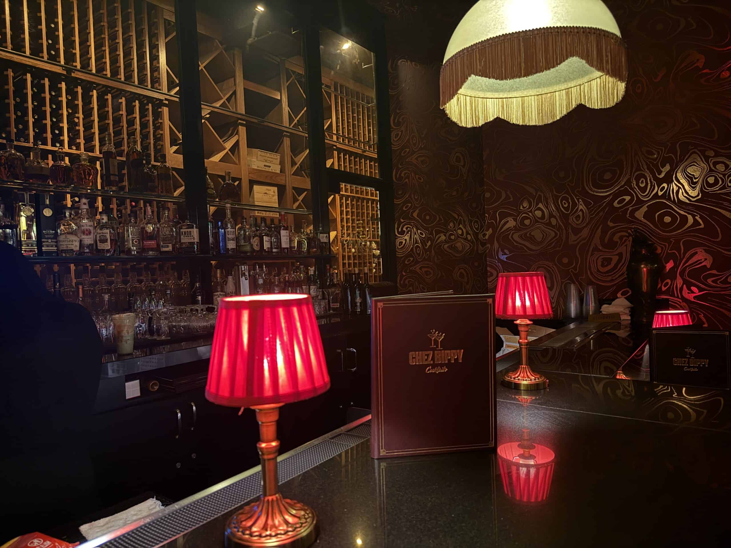 The bartop at Chez Bippy with red lamps, and an illuminated wine rack on the back wall.