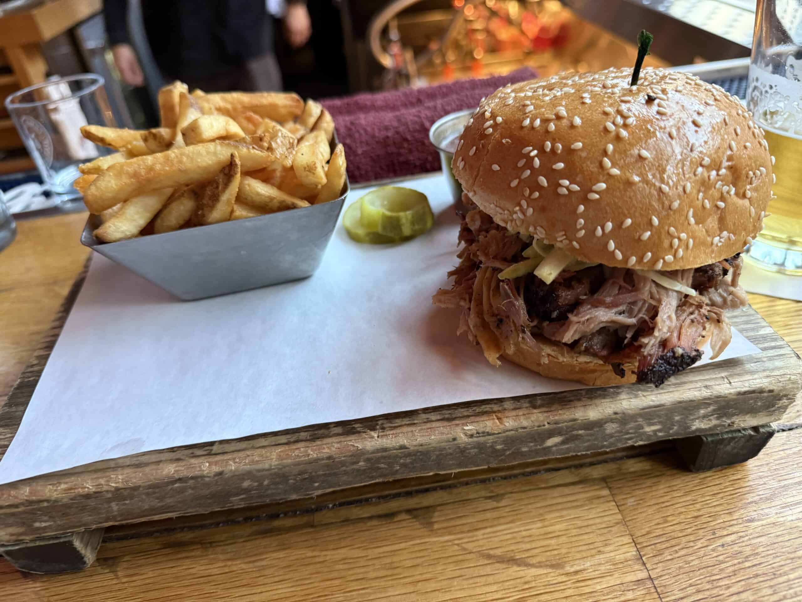 A pulled pork sandwich at Virgil's next to a cup of french fries.